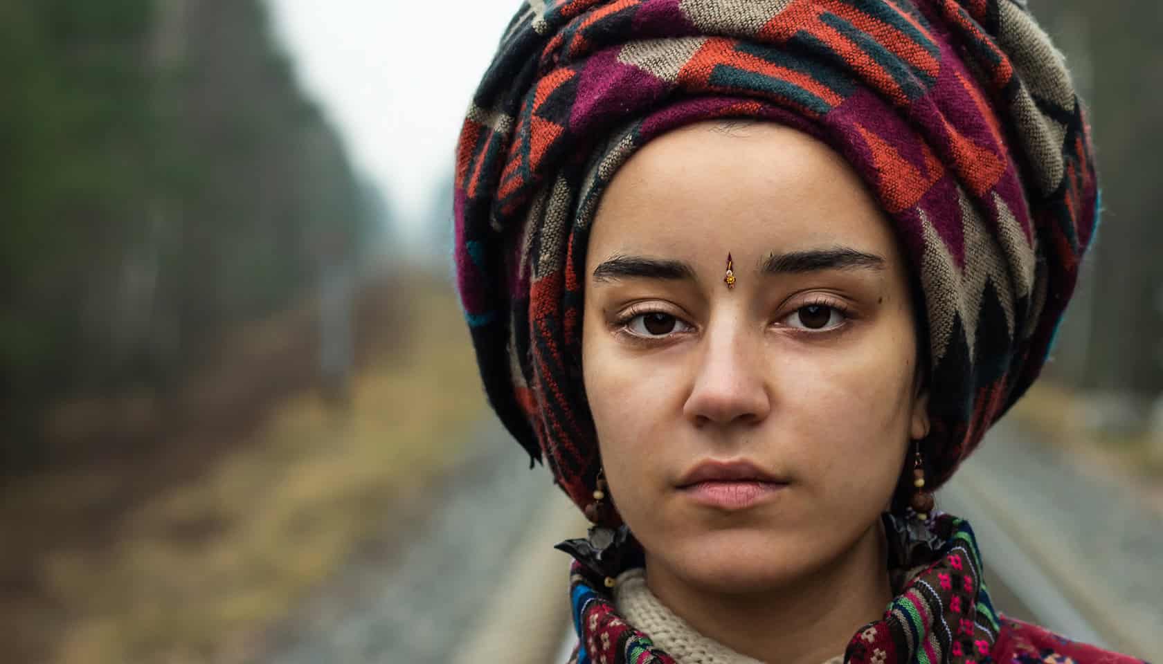 Intricate colorful headwrap worn by a young woman in a natural outdoor setting for cultural heritage.